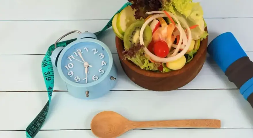 Réveil bleu, ruban à mesurer, salade fraîche et haltère bleu. L'heure est à la forme, jeune 16/8.