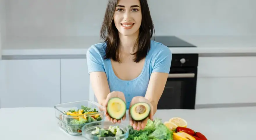Uśmiechnięta kobieta prezentuje awokado, składnik wielu diet, w tym keto. Jej opinie o keto diecie są pozytywne.