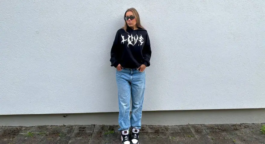 Dziewczyna w czarnej bluzie z kapturem i jeansach, idealny outfit, jak się ubrać na koncert hip hopowy.