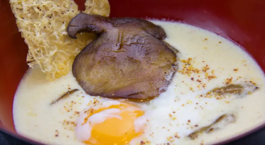 Un œuf parfait, crémeux et onctueux, baigne dans une soupe onctueuse, garnie d'un champignon poêlé et d'une tuile croustillante.