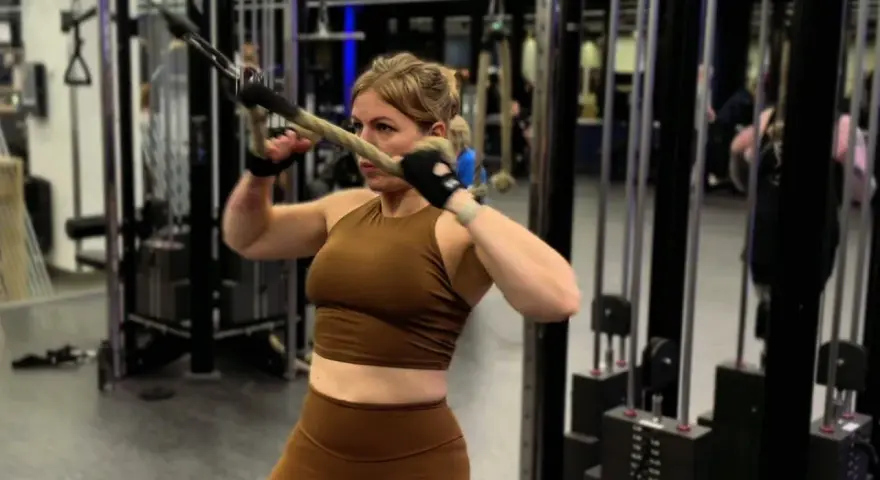 Kvinna utför stående rodd med kabelmaskin. Hon fokuserar på träningen i gymmet.