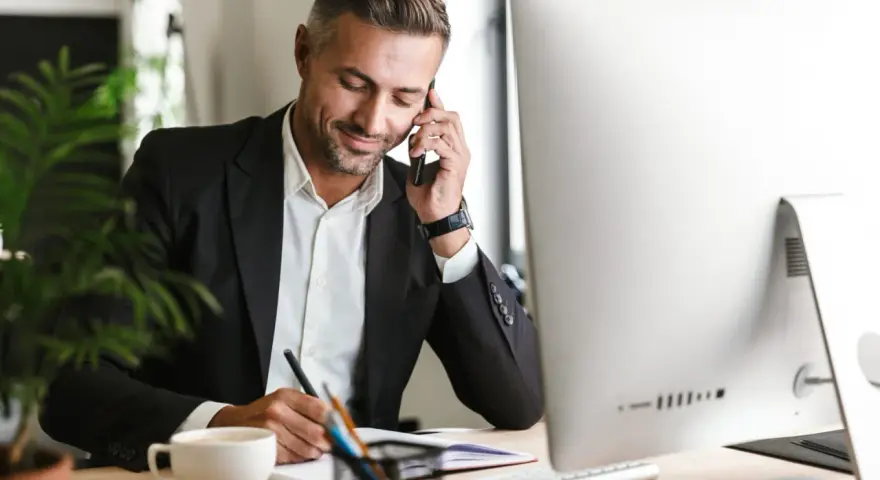 Uomo d'affari al telefono, scrive appunti. Potrebbe essere un agente immobiliare che discute di quanto guadagna un agente immobiliare.