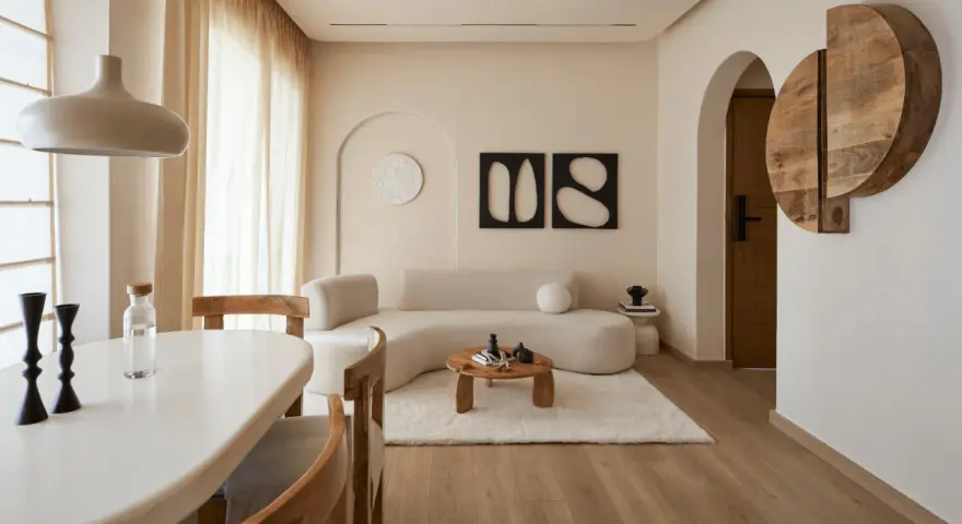 Un soggiorno in stile wabi sabi arredamento, con divano curvo, tavolino in legno grezzo, tappeto soffice e decorazioni organiche.