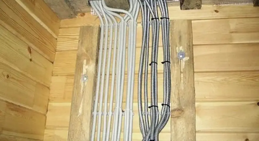 Instalacja elektryczna w domu drewnianym schemat: wiązki kabli w peszlach wychodzące z sufitu, przymocowane do drewnianych belek.