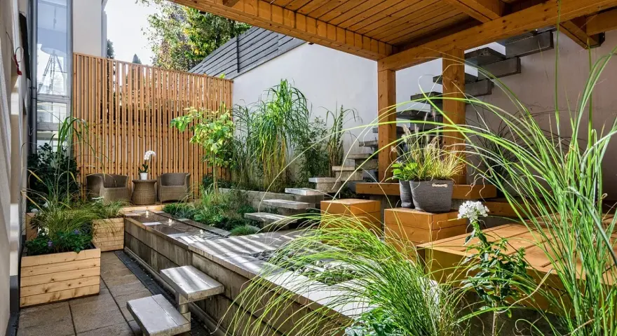 Giardini fioriti idee: un angolo zen con vasca d'acqua, gradini in pietra, sedute in legno e piante rigogliose sotto un pergolato.