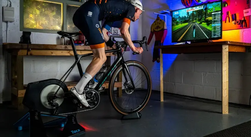 A cyclist trains indoors on a bike trainer, with a screen showing a virtual road. This setup demonstrates how to set up a bike trainer for immersive cycling.