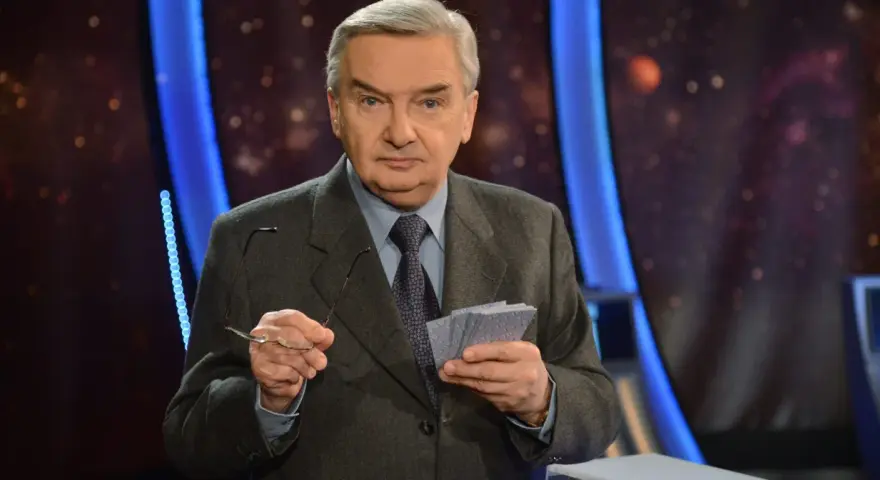 Starszy mężczyzna w garniturze trzyma okulary i karty z napisem "jeden z dziesięciu kiedy".