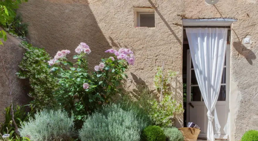 Lavendel beet ideen: Ein mediterraner Garten mit Rosen, Lavendel und einer Tür mit weißem Vorhang.