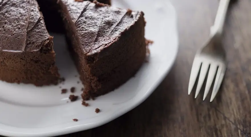 Una fetta di torta al cioccolato su un piatto bianco, con una forchetta accanto. Un'opzione deliziosa per chi cerca dolci senza zucchero.