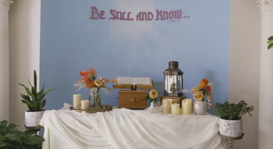 A serene scene for a midnight vigil: an open Bible, a lantern, and candles on a draped table, with "Be Still, and Know..." on the wall.