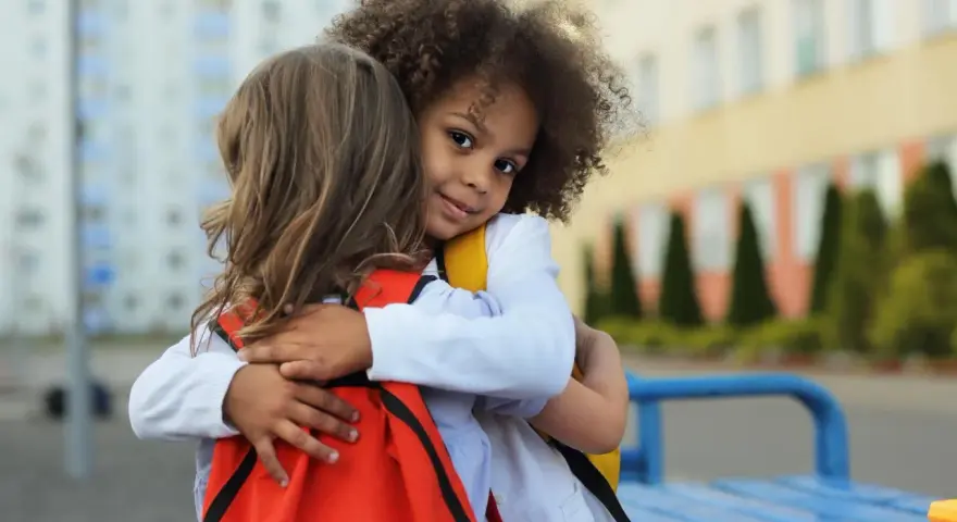 Zwei Kinder umarmen sich. Ein Mädchen mit Locken lächelt in die Kamera. Ein schönes Beispiel für Empathie bei Kindern.