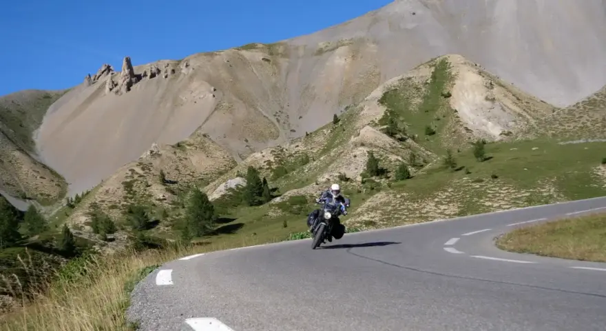 Motociclista percorre la route de grand alpes tra montagne scoscese e cielo azzurro.