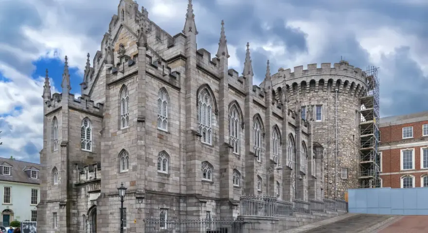 Kamienne mury i strzeliste wieże zdobią zamek w Dublinie. Gotycka architektura i chmurne niebo tworzą majestatyczny widok.