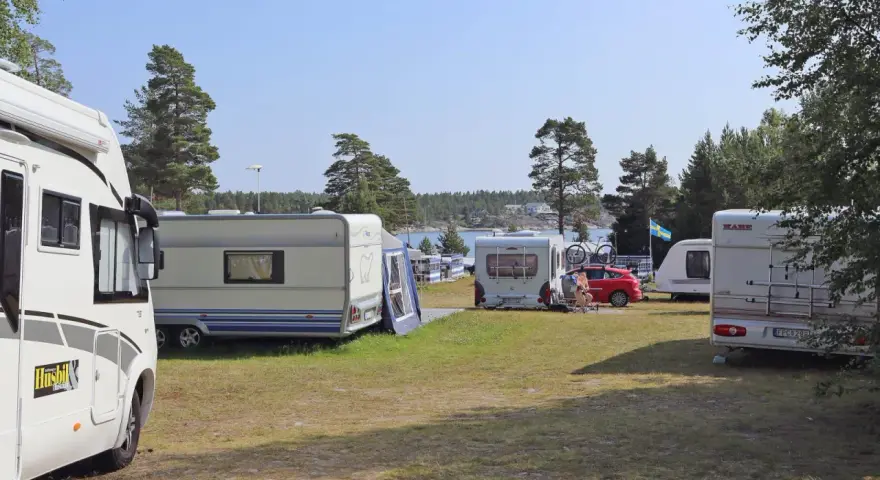 Solig dag på camping norrlandskusten med husbilar och husvagnar uppställda nära vattnet.