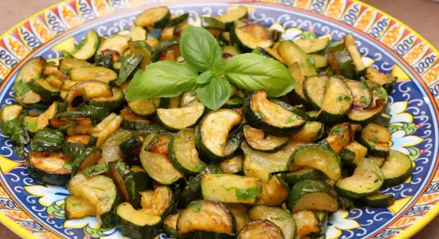 Zucchine trifolate dorate e saporite, guarnite con basilico fresco, servite su un piatto decorato.