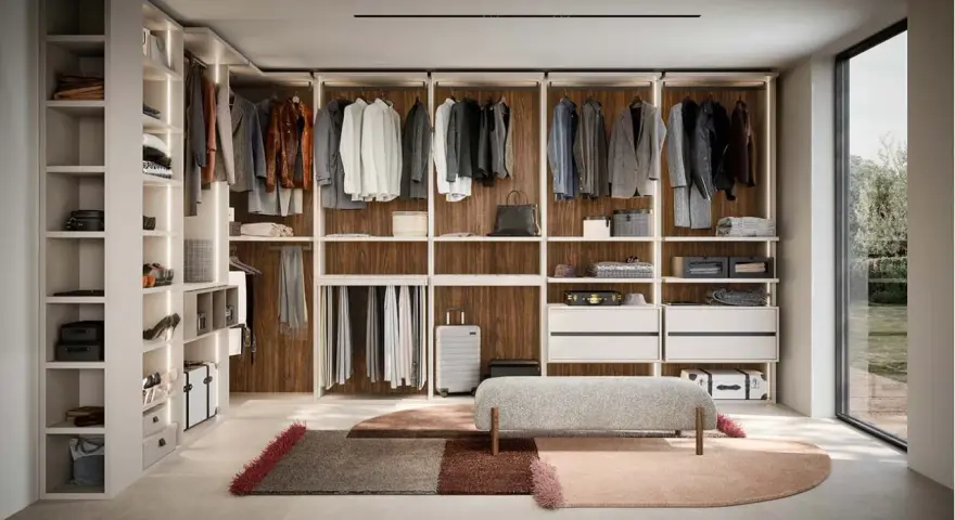 Ampia cabina armadio stanza con scaffali a vista, abiti appesi, cassettiere e un pouf centrale.