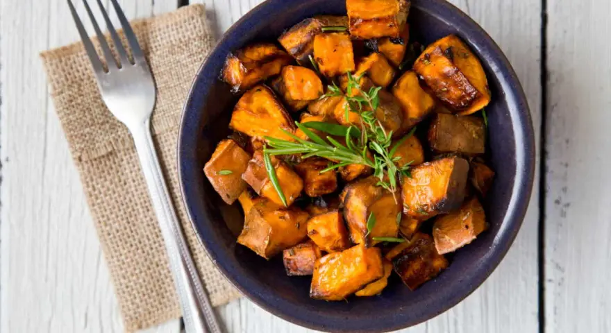 Patate douce air fryer croustillante, garnie d'herbes fraîches, servie dans un bol bleu avec une fourchette.