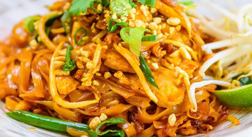 Un delicioso plato de pad thai con fideos de arroz, pollo, brotes de soja, cacahuetes picados y cilantro fresco.