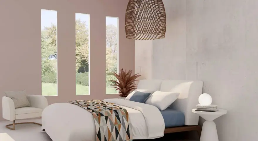 Habitación con cama blanca y manta geométrica. Tres ventanas verticales dejan ver un jardín. El espacio, con tonos neutros, evoca la serenidad de los cuartos blancos.
