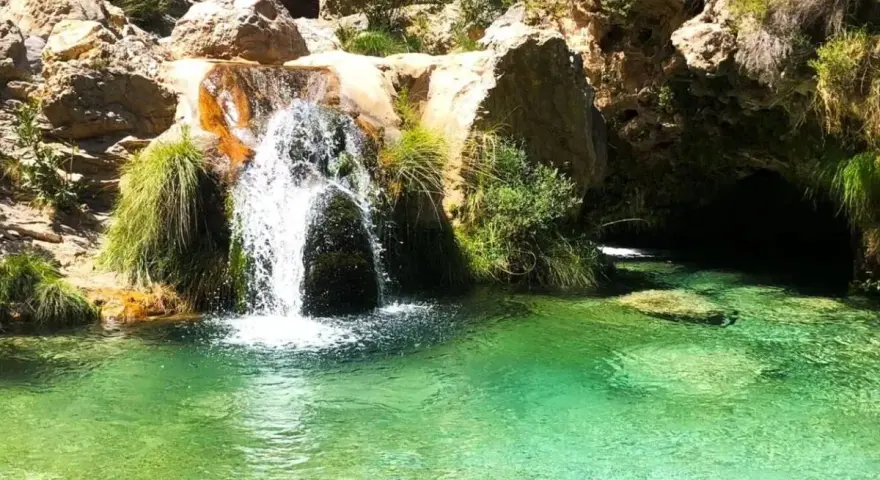 Cascada de agua cristalina cayendo en unas pozas turquesas, rodeadas de rocas y vegetación exuberante.