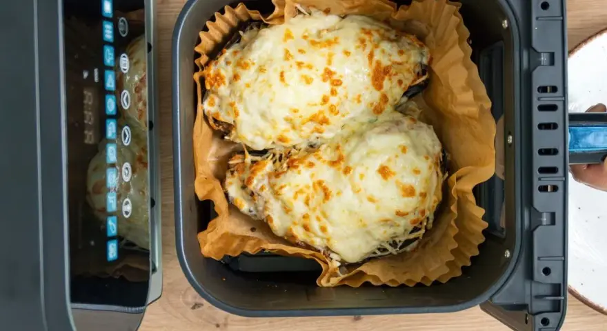 Dos mitades de berenjenas gratinadas con queso fundido, listas para disfrutar, recién salidas de la freidora de aire.