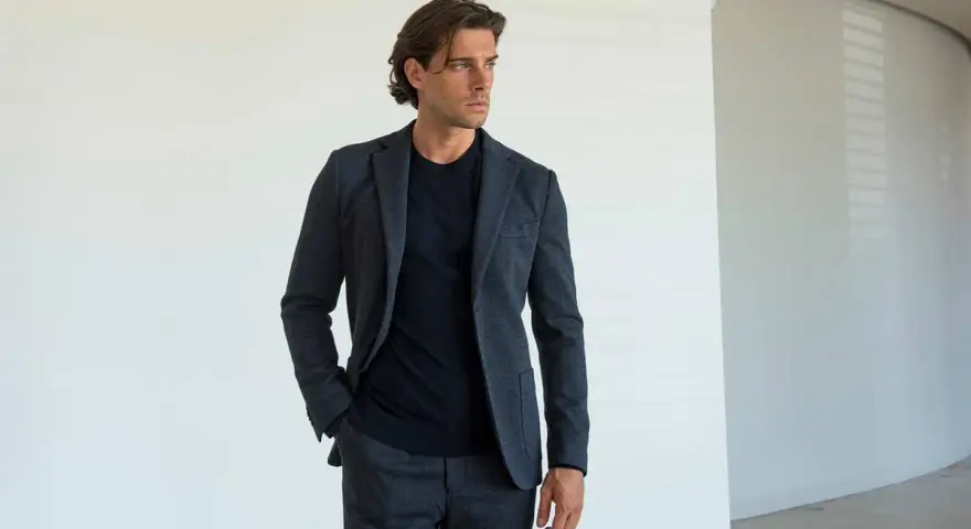 Uomo con giacca e pantaloni grigi, una mano nella tasca laterale del pantalone, mostrando i diversi tipi di tasche pantaloni uomo.