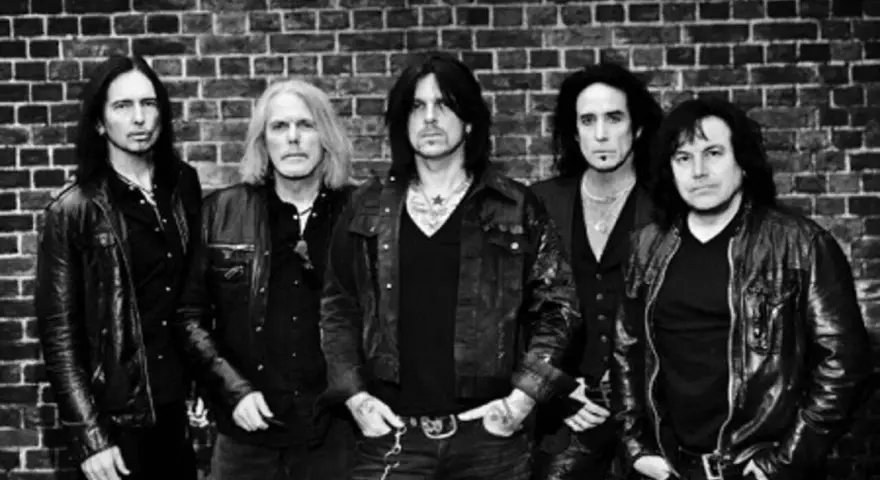 Les membres de Black Star Riders posent devant un mur de briques.