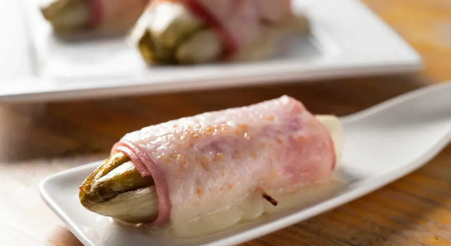 Endives au jambon sans béchamel, une recette simple et savoureuse. L'endive fondante enroulée de jambon sur une cuillère blanche.