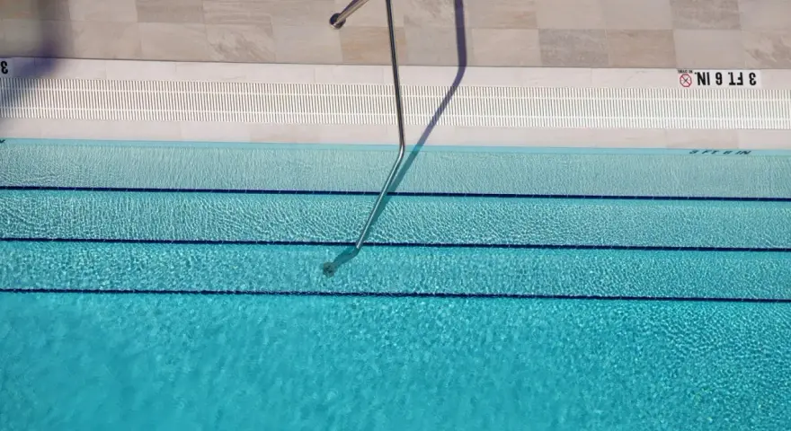Escalera metálica en piscina de agua clara, con marcas de profundidad. El mantenimiento de piscinas es clave para su disfrute.
