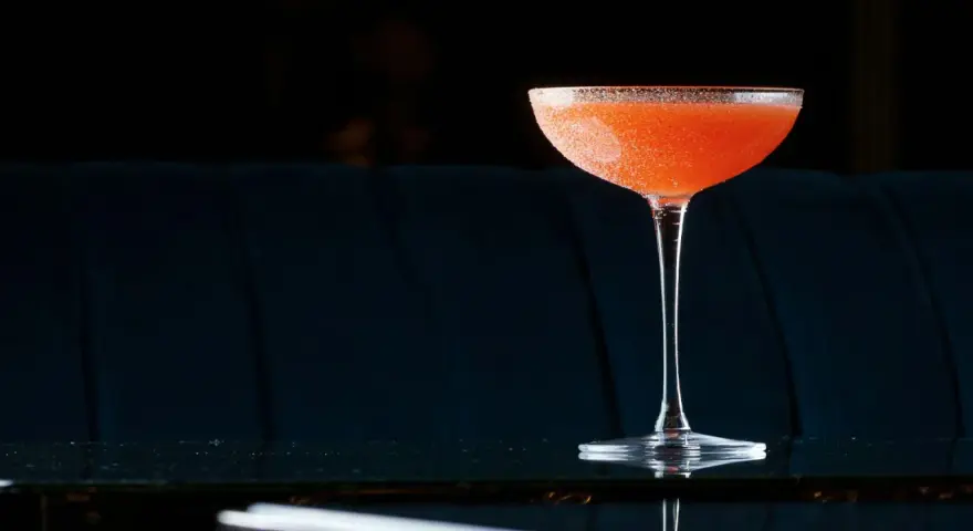 Orzeźwiający el presidente cocktail, z pomarańczowym odcieniem i cukrową obrączką, stoi na błyszczącym blacie.