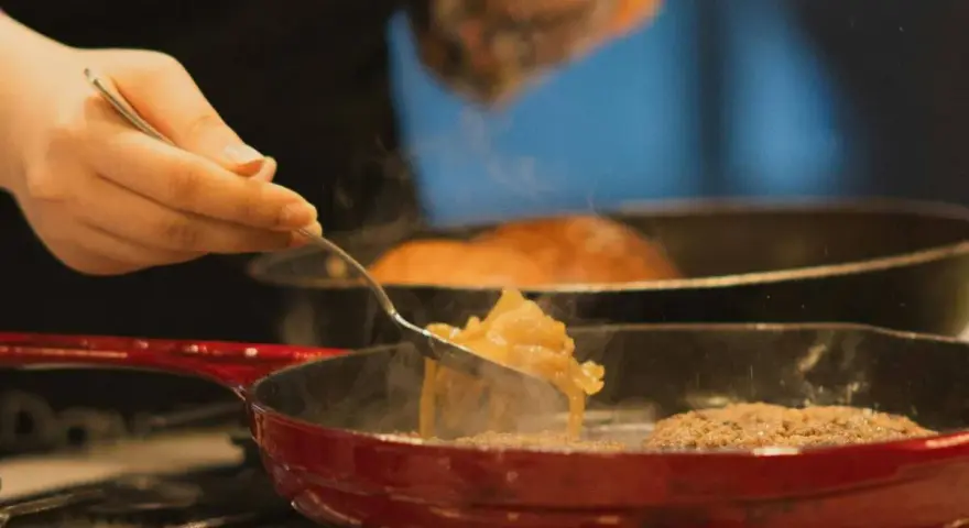 Cebolla caramelizada siendo removida con un tenedor en una sartén roja sobre el fuego.