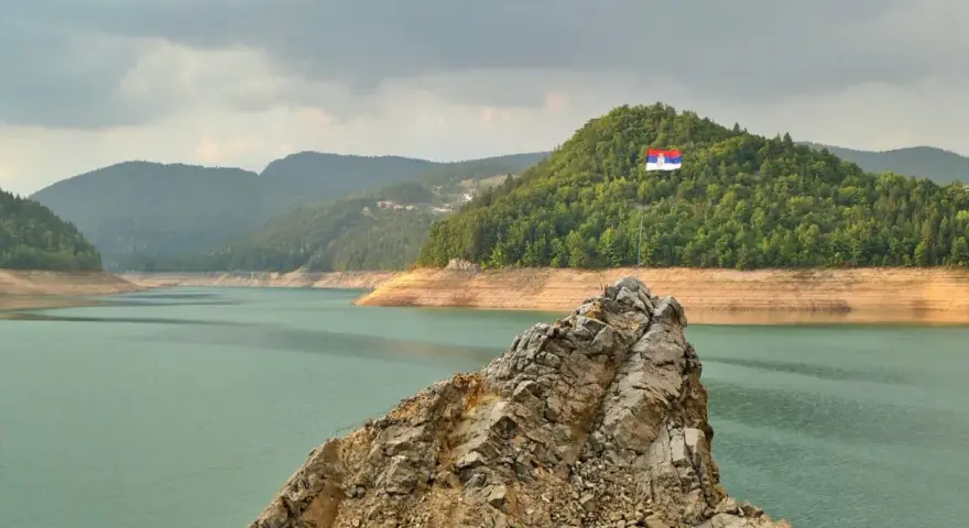 Serbska flaga na skale nad jeziorem. Krajobraz zachęca do podróży, a pytanie "czy Serbia jest bezpieczna dla turystów" wydaje się nie mieć znaczenia w obliczu tego spokoju.