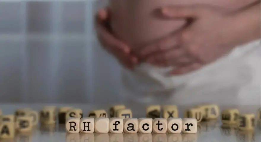 Ciąża i czynnik Rh. W tle brzuch kobiety, na pierwszym planie kostki z napisem "RH factor". Immunoglobulina w ciąży może być kluczowa.