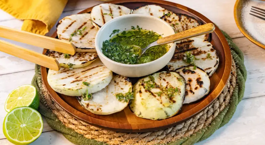 Gegrillte Kohlrabi-Scheiben mit Kräuter-Dressing und Limettenspalten auf einem Holzteller. Ein köstliches Gericht, das Lust auf Kohlrabi grillen macht.