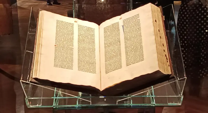 Otwarta biblia gutenberga pelplin, prezentowana na szklanym stojaku, świadectwo historii druku.