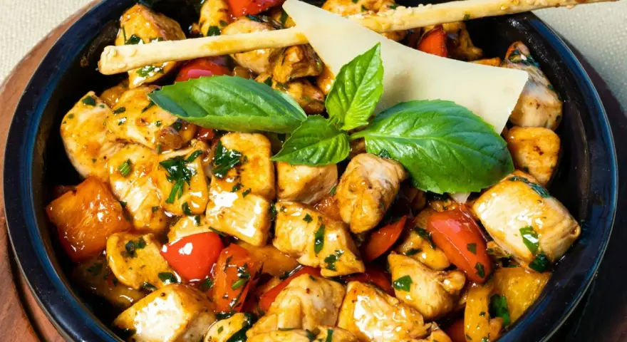 Kawałki kurczaka w sosie z papryką i ziołami, ozdobione listkami bazylii i paluszkami grissini. Danie przypomina egzotyczne jungle curry.