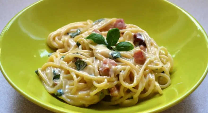 Spaghetti carbonara ze śmietaną, podane w zielonej misce, udekorowane bazylią. Pyszny przepis na klasyczne danie.