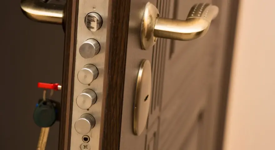 Poignée de porte blindée avec plusieurs serrures et une clé rouge. Des marques sur le cylindre supérieur suggèrent une tentative d'effraction.