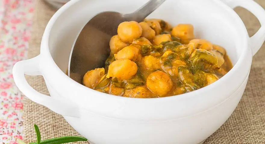 Un tazón blanco lleno de garbanzos con acelgas, un plato reconfortante y nutritivo.