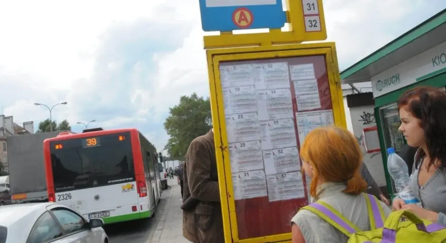 Ludzie sprawdzają 79 rozkład jazdy na przystanku. Autobus linii 39 stoi obok.
