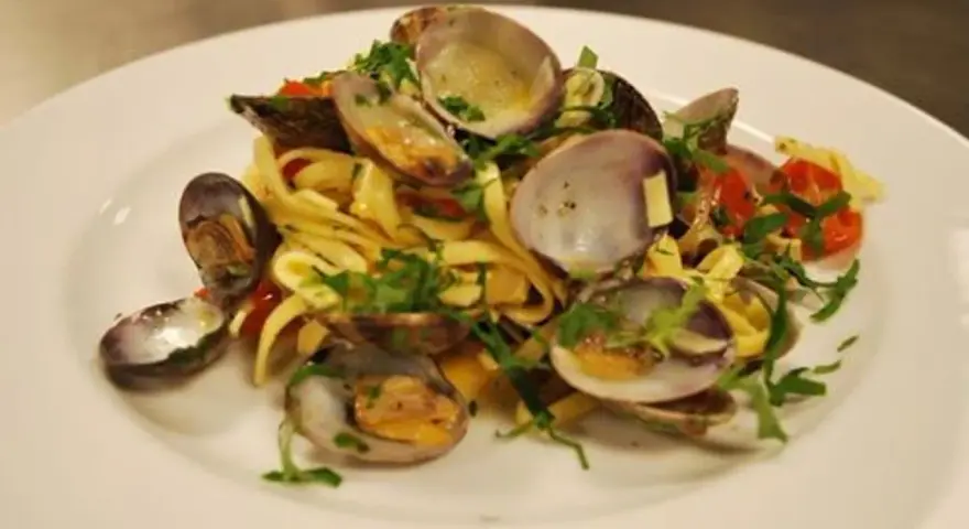 En tallrik med pasta vongole, där färska vongole-musslor blandas med tagliatelle, körsbärstomater och persilja.