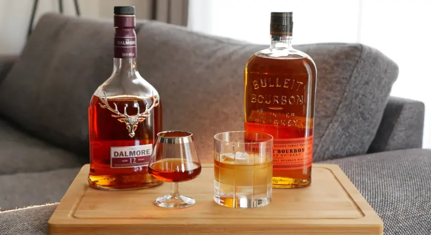 Zwei Flaschen edler Tropfen: Dalmore Scotch und Bulleit Bourbon. Ein Glas Scotch und ein Glas Bourbon mit Eis stehen bereit.