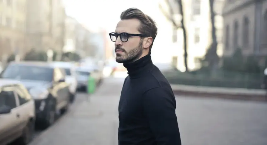 Elegancki mężczyzna w czarnym golfie i okularach, zamyślony, jakby planował zagrywki zakochanego faceta.