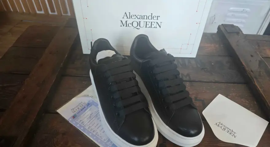 Czarne sneakersy Alexander McQueen na grubej, białej podeszwie, obok pudełka z logo marki.