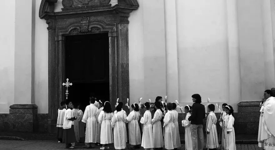 Dzieci w albach czekają przed kościołem, kiedy sa komunie. Trzymają świece, gotowe na uroczystość.