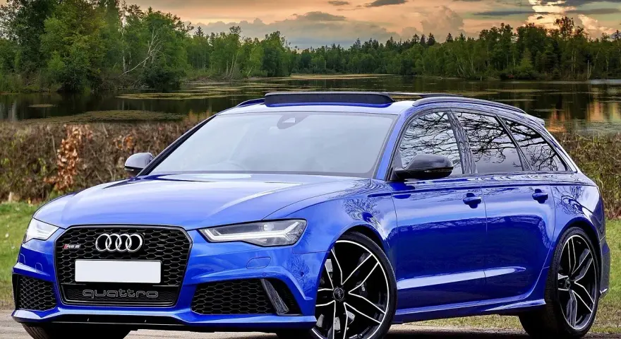 Niebieski **hatchback** z napędem quattro, zaparkowany nad jeziorem, z pięknym zachodem słońca w tle.
