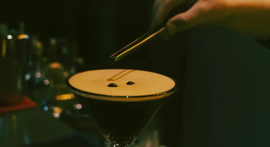 En hand lägger kaffebönor på en krämig espresso martini.