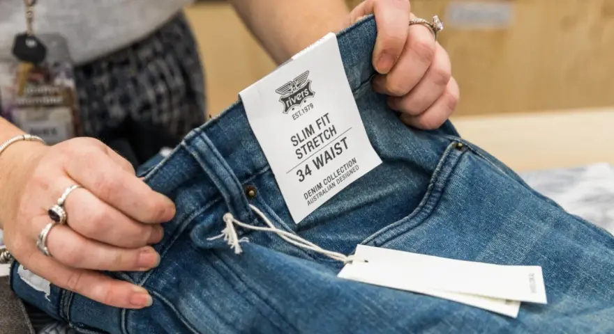 Dłonie trzymają dżinsy z metką "SLIM FIT STRETCH 34 WAIST". Czy to dobry rozmiar?