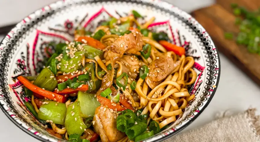 En skål med kycklingwok med nudlar, grönsaker och sesamfrön. En härlig och färgstark måltid.