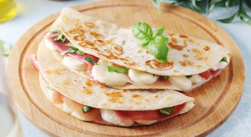 Piadina come farcirla: prosciutto, mozzarella filante e basilico fresco, un'idea gustosa e veloce.